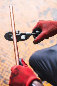 Plombier Expert | Homme avec gants rouges coupant un tuyaux
